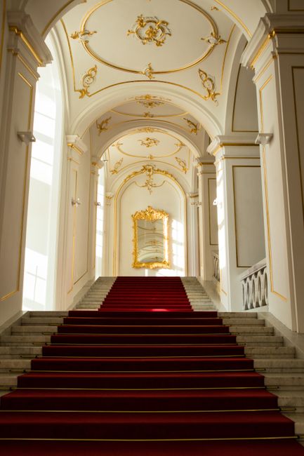 Majestic staircase with red carpet in a historic building, featuring ornate decor.