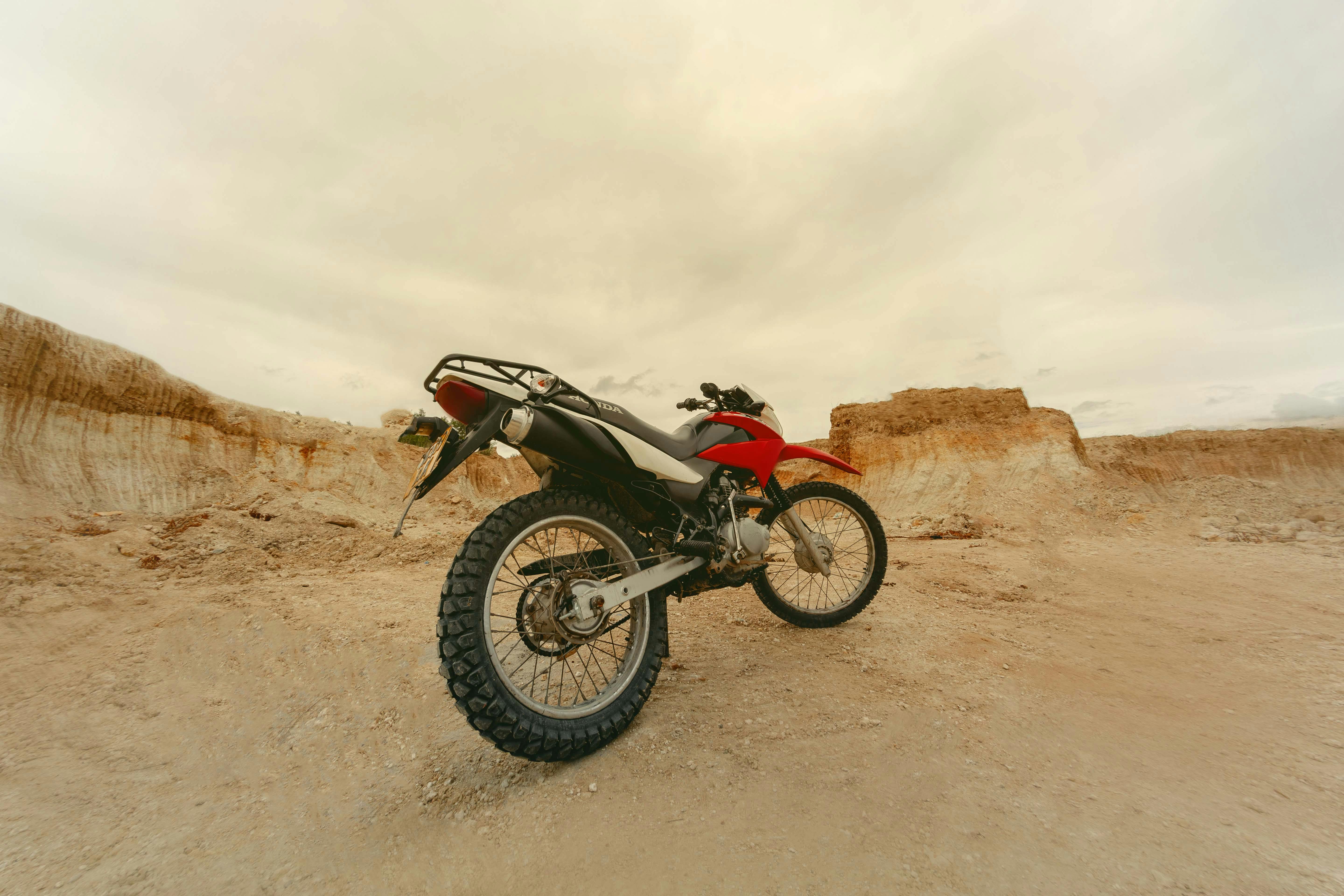 Red motorbike on rugged desert terrain, ideal for adventure travel imagery.