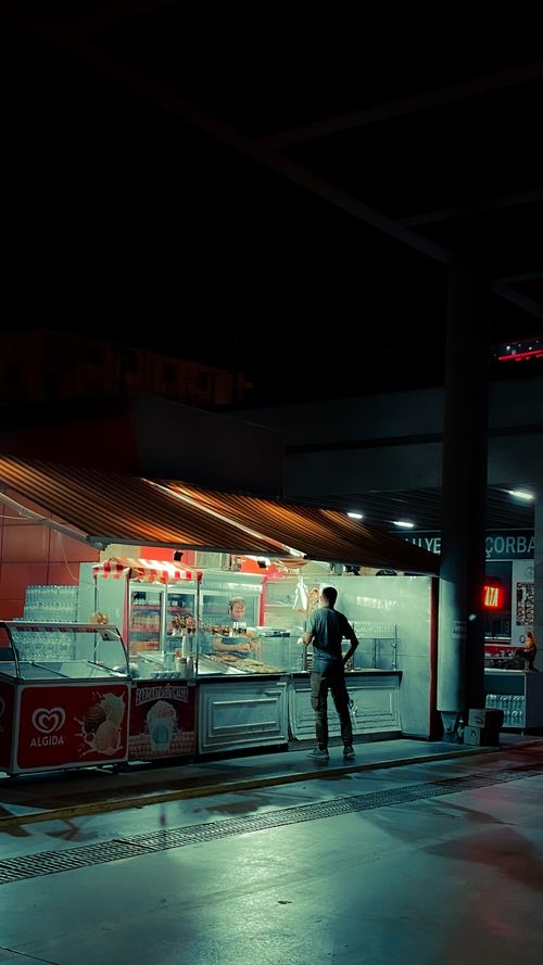 Free A man stands at a street food stall in a dimly lit urban setting at night. Stock Photo