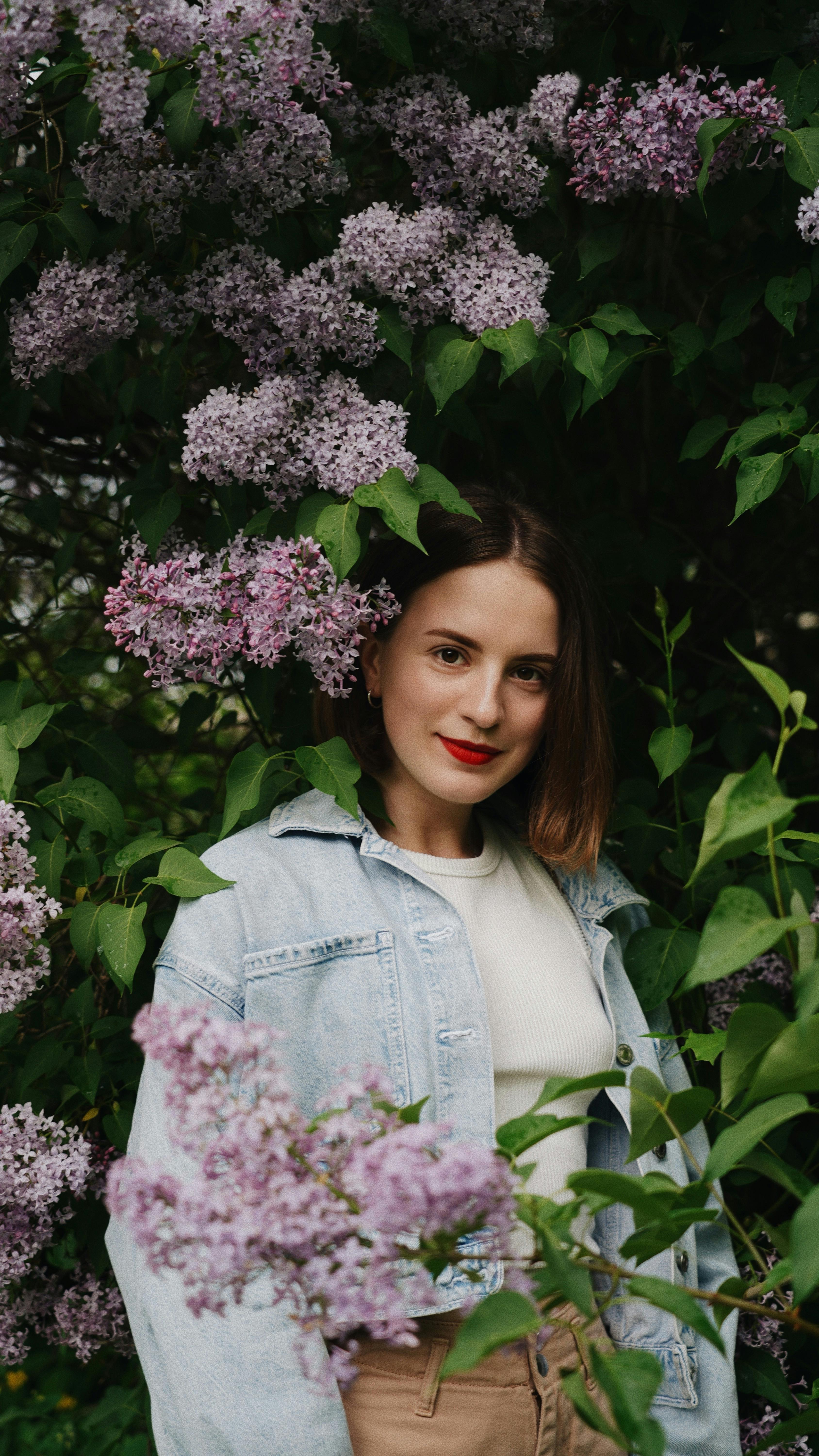 Portrait of a woman in a denim jacket surrounded by vibrant lilac flowers.