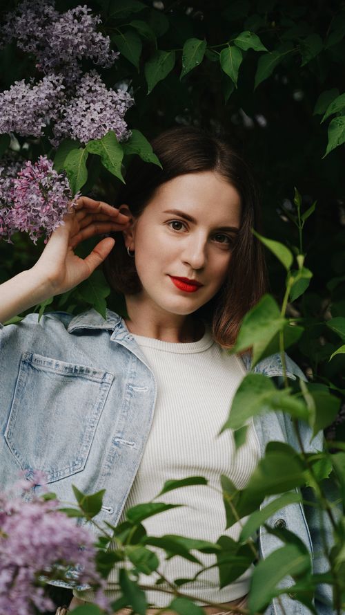 Free Portrait of a woman in a jean jacket surrounded by blooming lilac flowers outdoors. Stock Photo