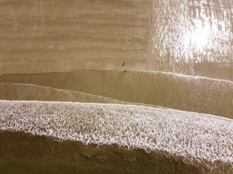 A stunning aerial perspective of a sandy beach with overlapping waves and unique sand patterns.
