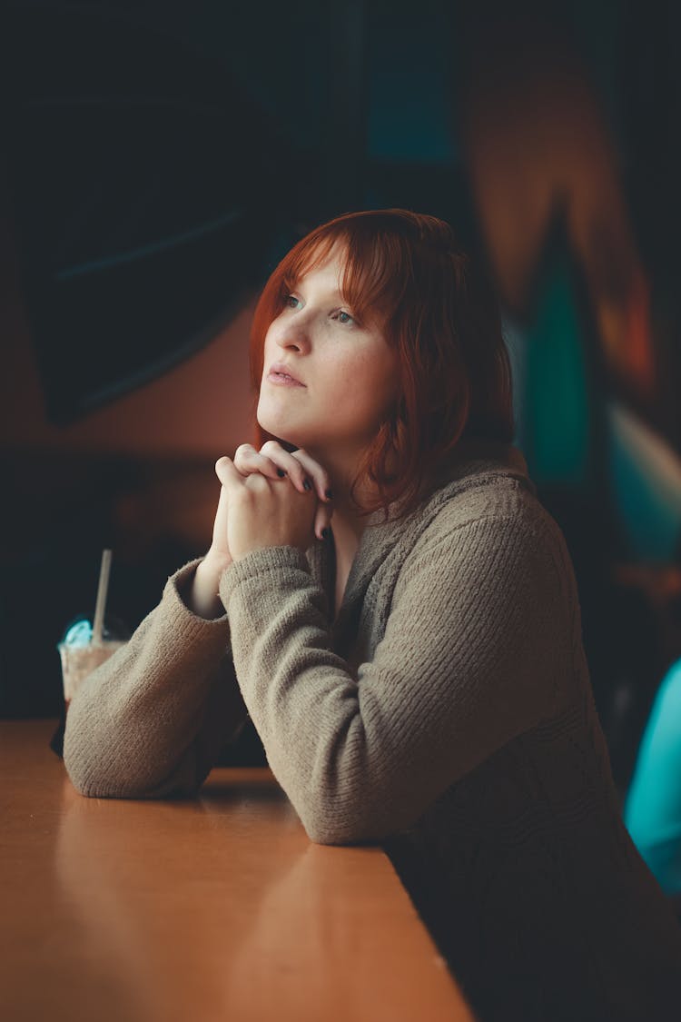 Girl With Long Ginger Hair Sitting At Table With Hands Clasped