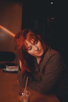 Charming redhead woman in a cafe, enjoying a relaxed moment with a drink.