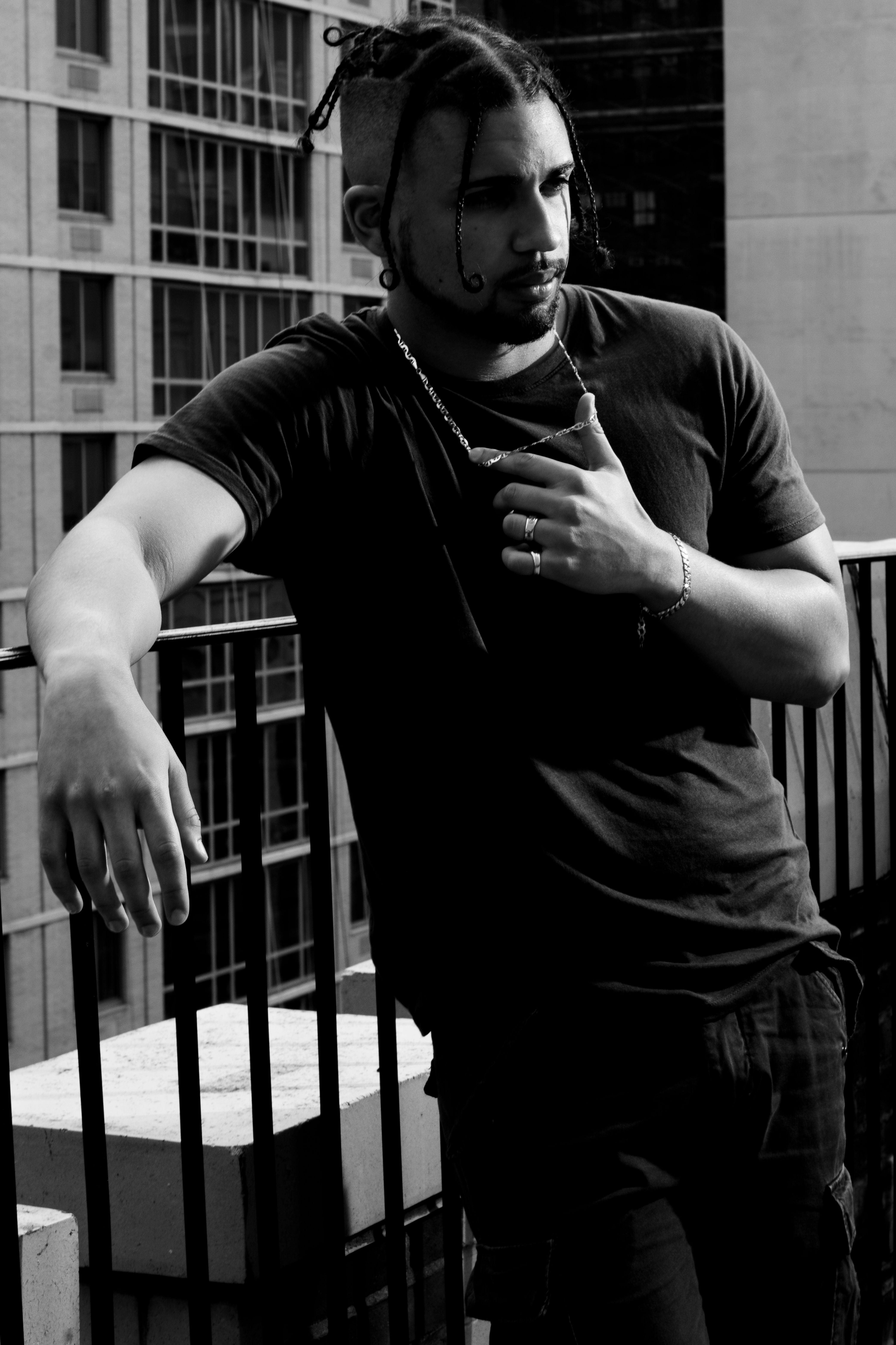 Stylish black and white portrait of a man standing on a city balcony, exuding urban sophistication.