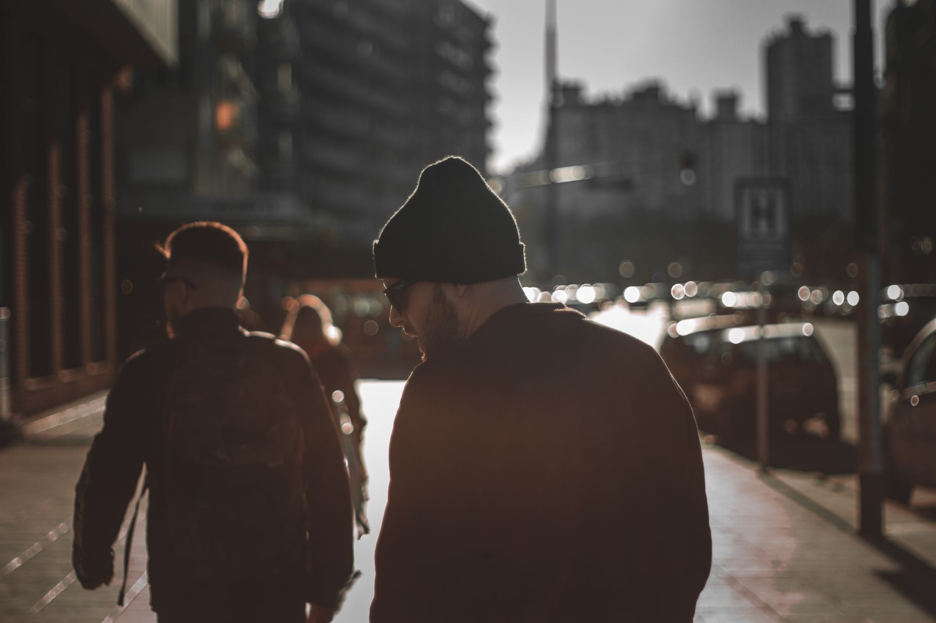Homme bonnet noir style grunge urbain marchant dans une rue animée au coucher du soleil