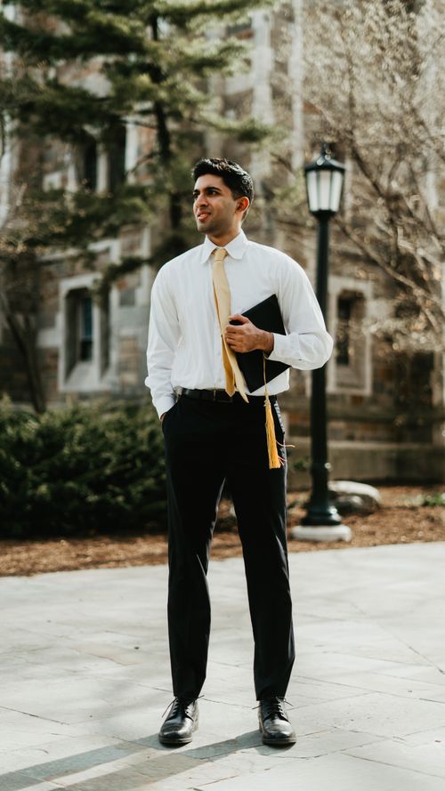 Free Young man standing outdoors in graduation attire holding his cap, showcasing success. Stock Photo
