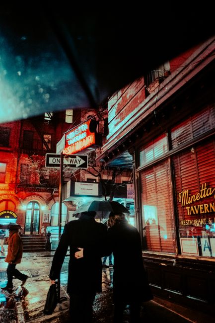 Wet streets of a city at night with pedestrians and neon lights reflecting in puddles.
