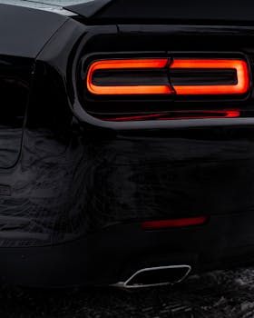 Close-up of a black sports car's rear with glowing taillights, showcasing modern design.