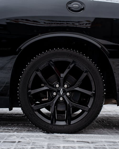 Wheel of a Black Car with a Winter Tire on a Snow-covered Driveway
