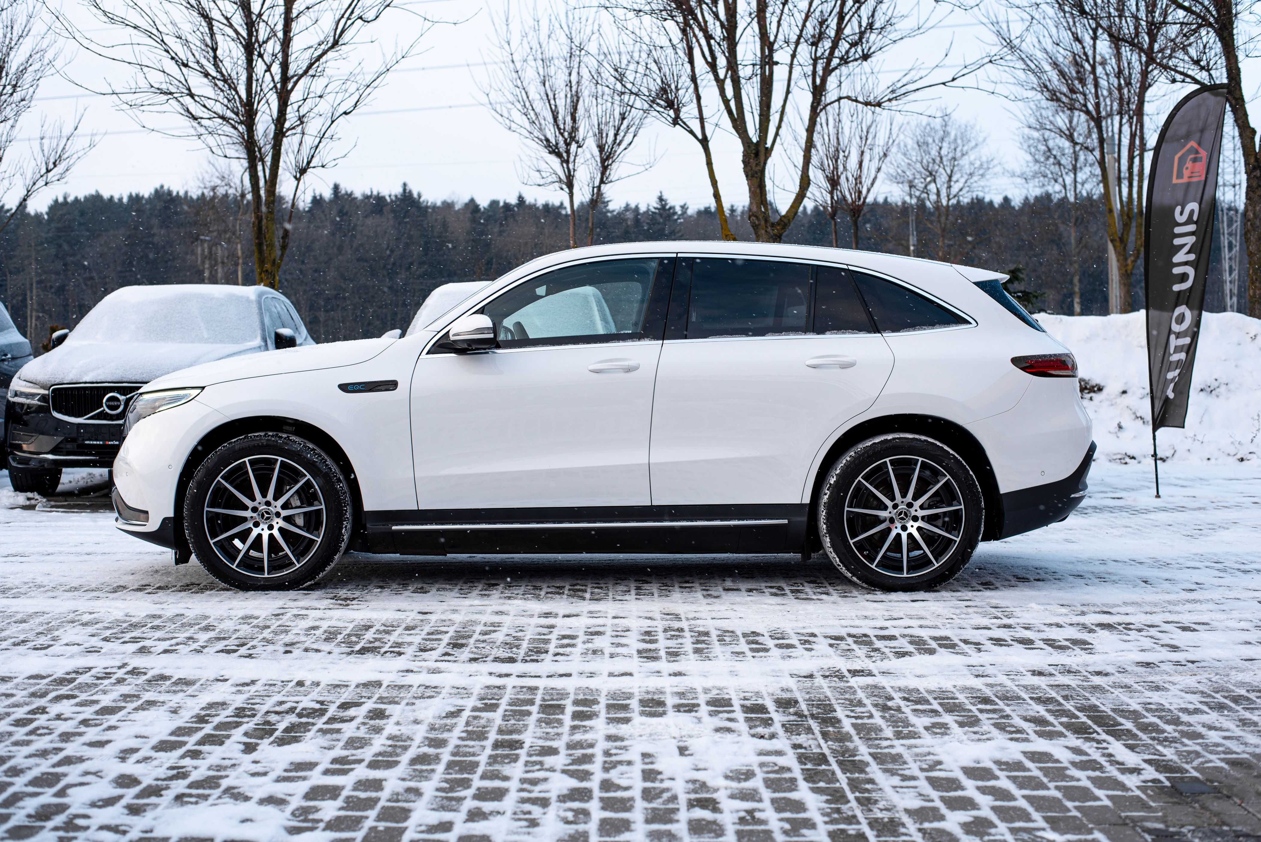 White luxury SUV parked on a snowy paved road, surrounded by winter trees.