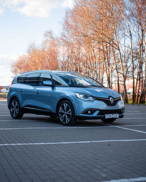 Free A shiny blue Renault car parked in an empty lot with bare trees in the background. Stock Photo