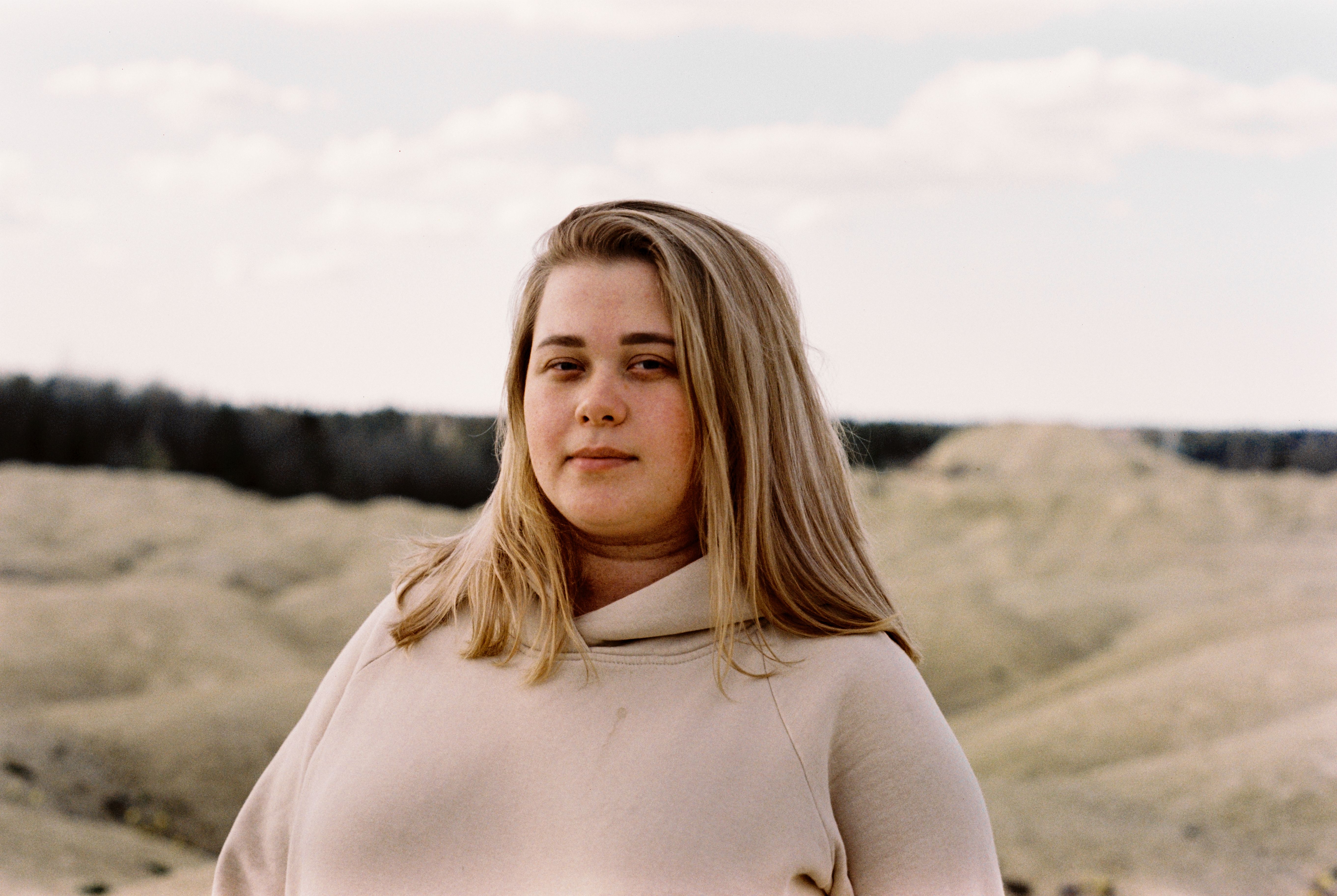 A serene portrait of a woman in a beige hoodie with a natural outdoor background.
