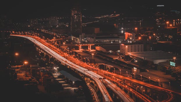 Dynamic aerial view of an urban highway at night with vibrant light trails creating a lively cityscape.