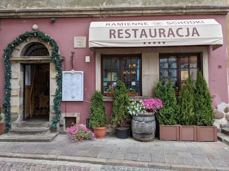 Street view of a classic restaurant facade in Poland adorned with plants and flowers.