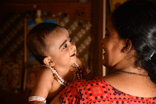 Free A heartwarming scene of a mother holding and smiling at her baby in a traditional setting. Stock Photo