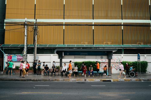 Free A diverse group of people waiting at a bus stop in an urban setting, some wearing masks. Stock Photo