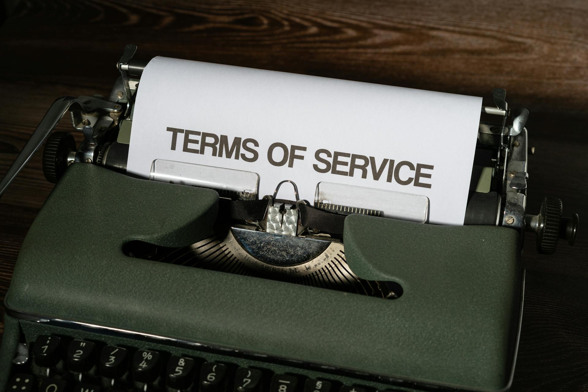 Close-up of a vintage typewriter with 'Terms of Service' paper inside, on a wooden desk.