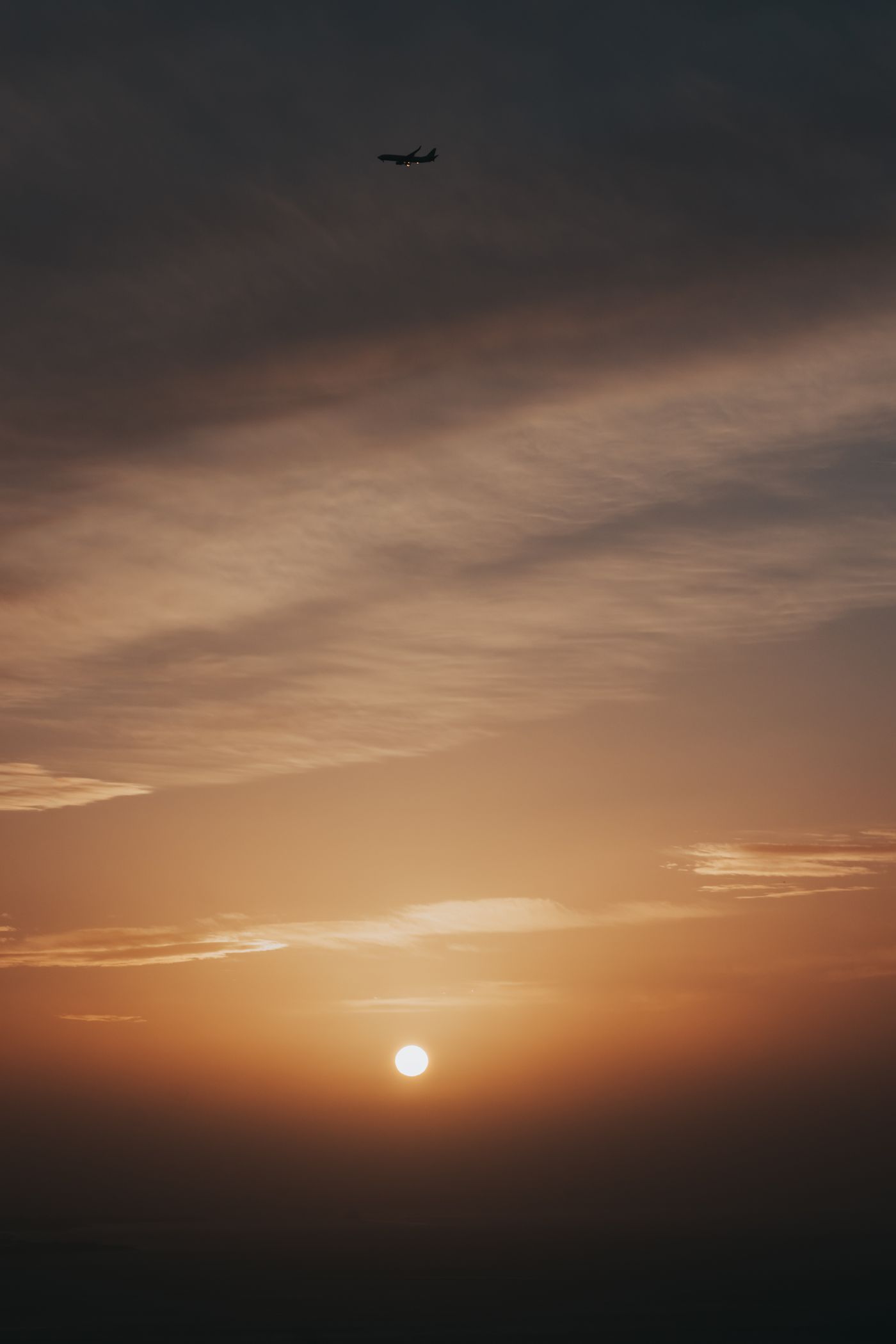 Silhouette of an airplane climbing above the clouds during a dramatic sunset