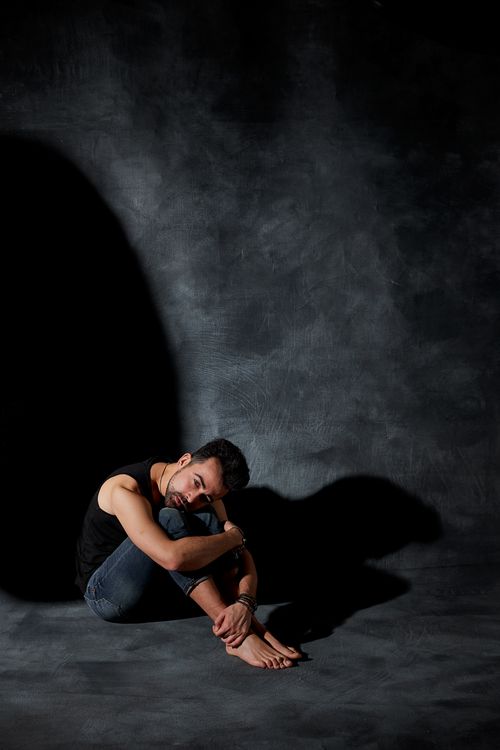 Free A solitary man sits barefoot on a dark concrete floor, exuding a sense of introspection and solitude. Stock Photo