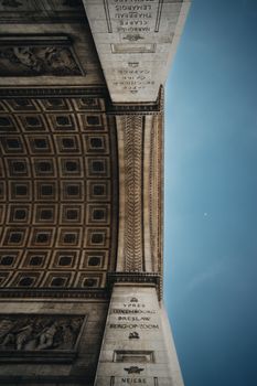 Low angle shot of Arc de Triomphe, Paris, showcasing detailed ceiling against a clear blue sky.