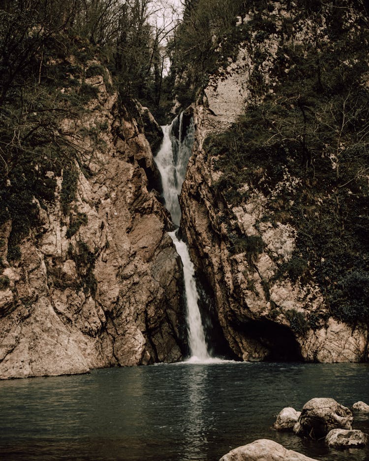 Waterfall Running From Top Of Rocks In Forest To Lake