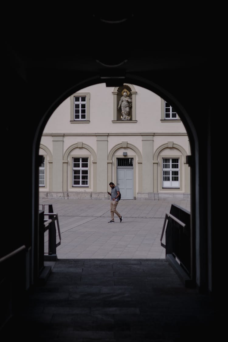 A Man Walking In The Street Near The Arched Doorway