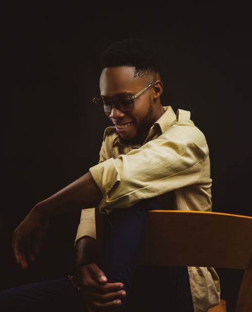 Free Portrait of a smiling man with eyeglasses, sitting on a wooden chair against a dark background. Stock Photo