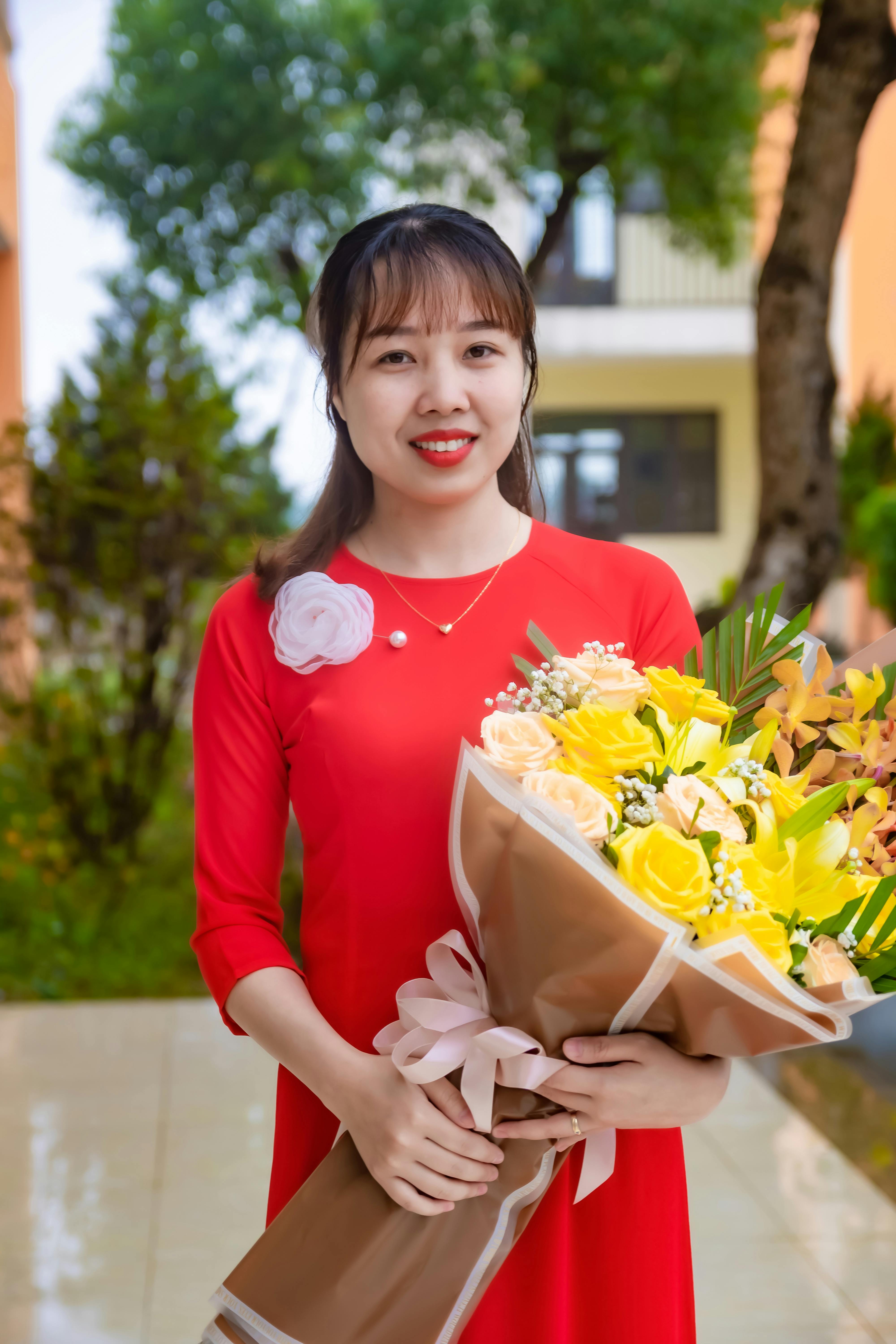 An Asian woman in a red dress smiles while holding a vibrant bouquet of yellow flowers outdoors.