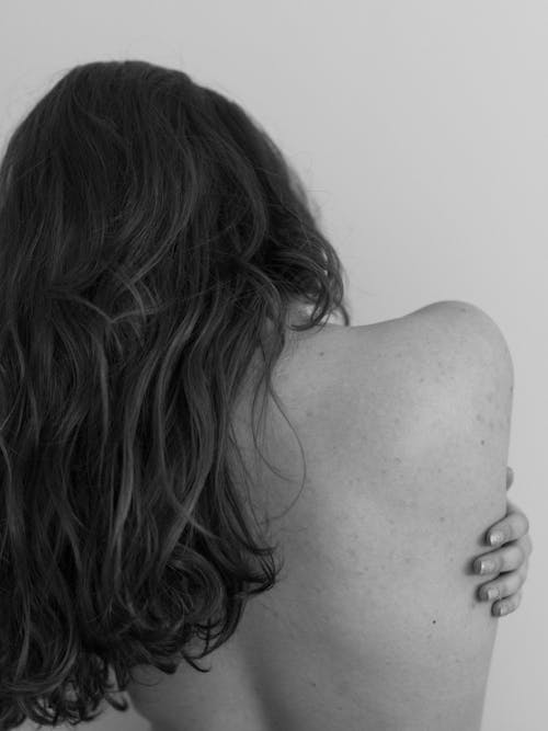 A Back View of a Topless Woman Touching Her Back