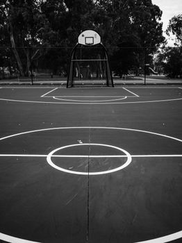 A minimalist black and white image of an empty outdoor basketball court. Perfect for sports themes.