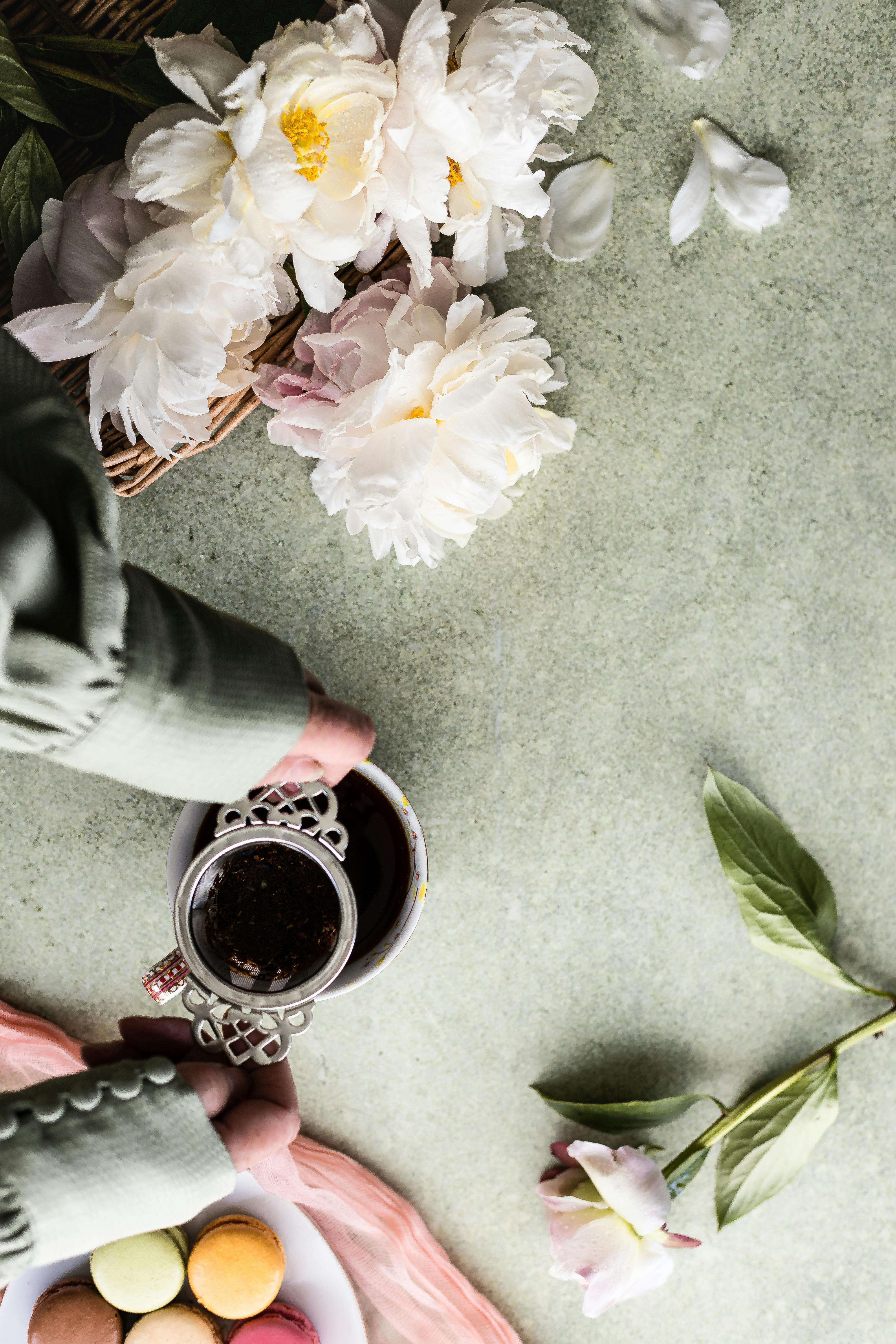 A serene tea flat lay with white peonies and colorful macarons on a concrete table.