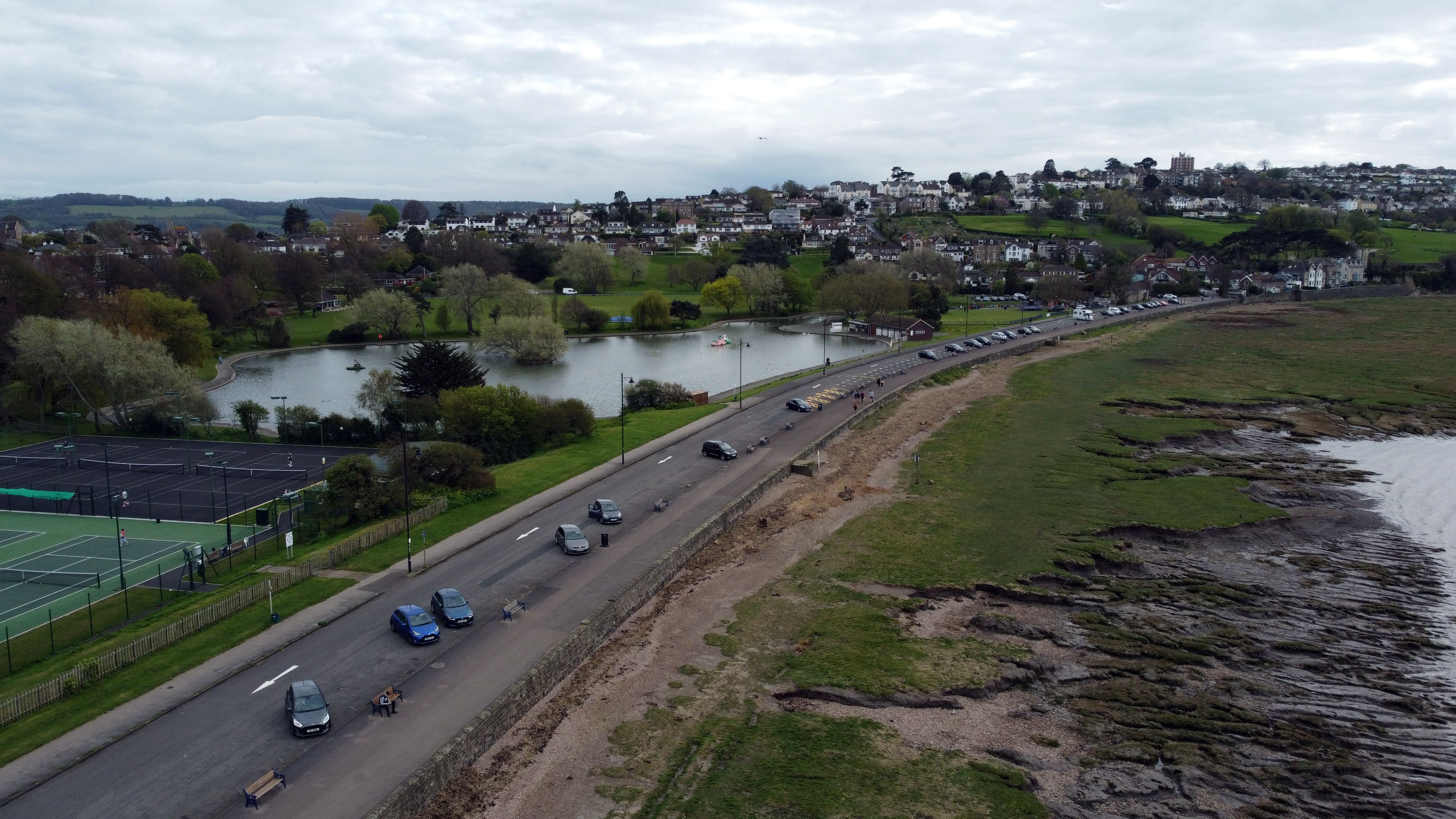 Drone shot capturing the scenic landscape of Portishead, England with road, lake, and tennis courts in view.