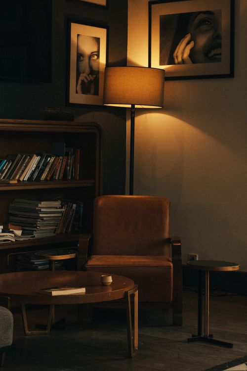 Free A warm, inviting room featuring bookshelves, a leather chair, and artistic frames. Stock Photo