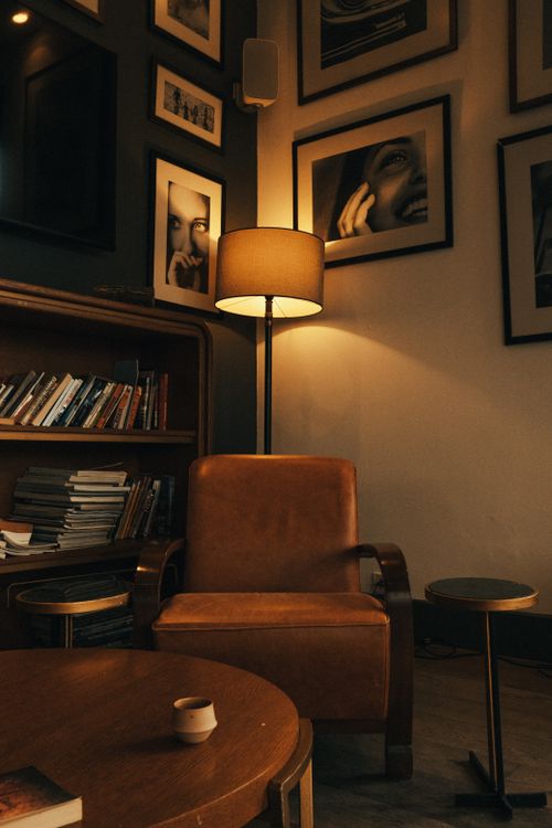 Free Warm and inviting room with a leather armchair, floor lamp, and art-filled walls. Stock Photo