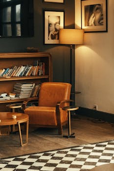 Warm and stylish interior featuring a leather armchair, standing lamp, and bookshelf with photos.