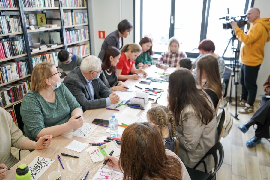 People seated around a table working together with paper and colouring materials in a community session.