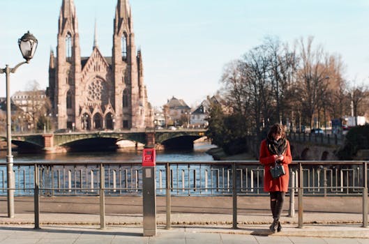 A woman standing by a river bridge near the Strasbourg Cathedral during a sunny day.
