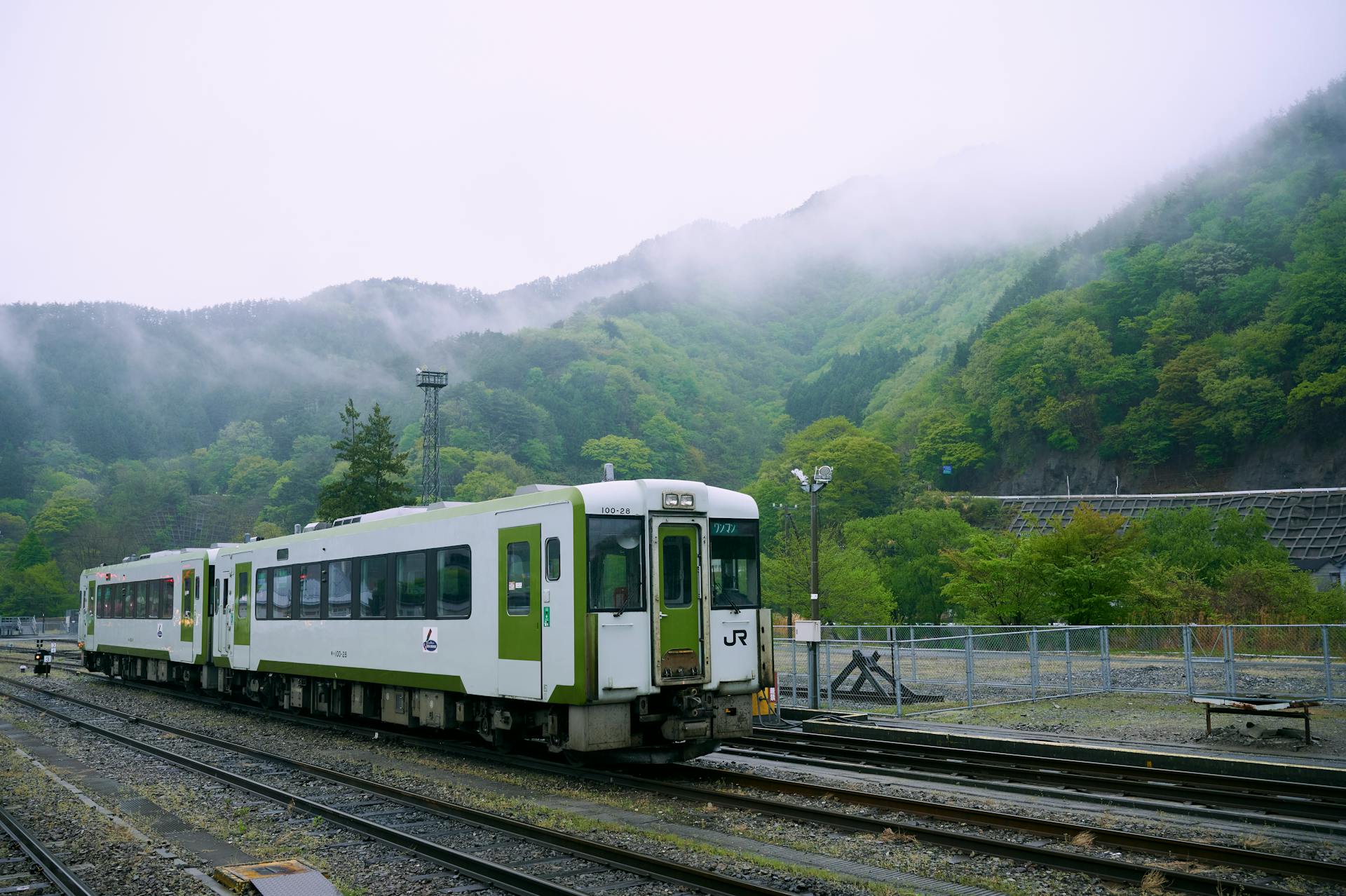 Train on tracks in Kamaishi, Japan with misty green mountains in the background, capturing serene travel vibes.