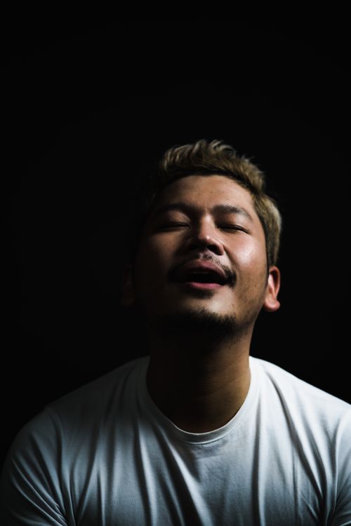 Free A dramatic portrait of a man in a white shirt with eyes closed against a black background. Stock Photo