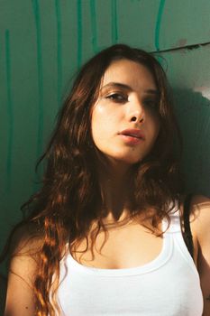 Close-up portrait of a brunette woman wearing a white tank top against a green background.