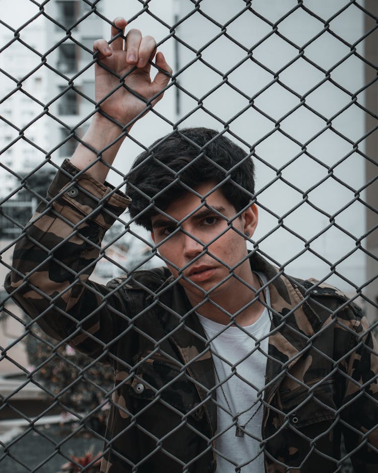 A Man In Camouflage Jacket Behind The Metal Fence