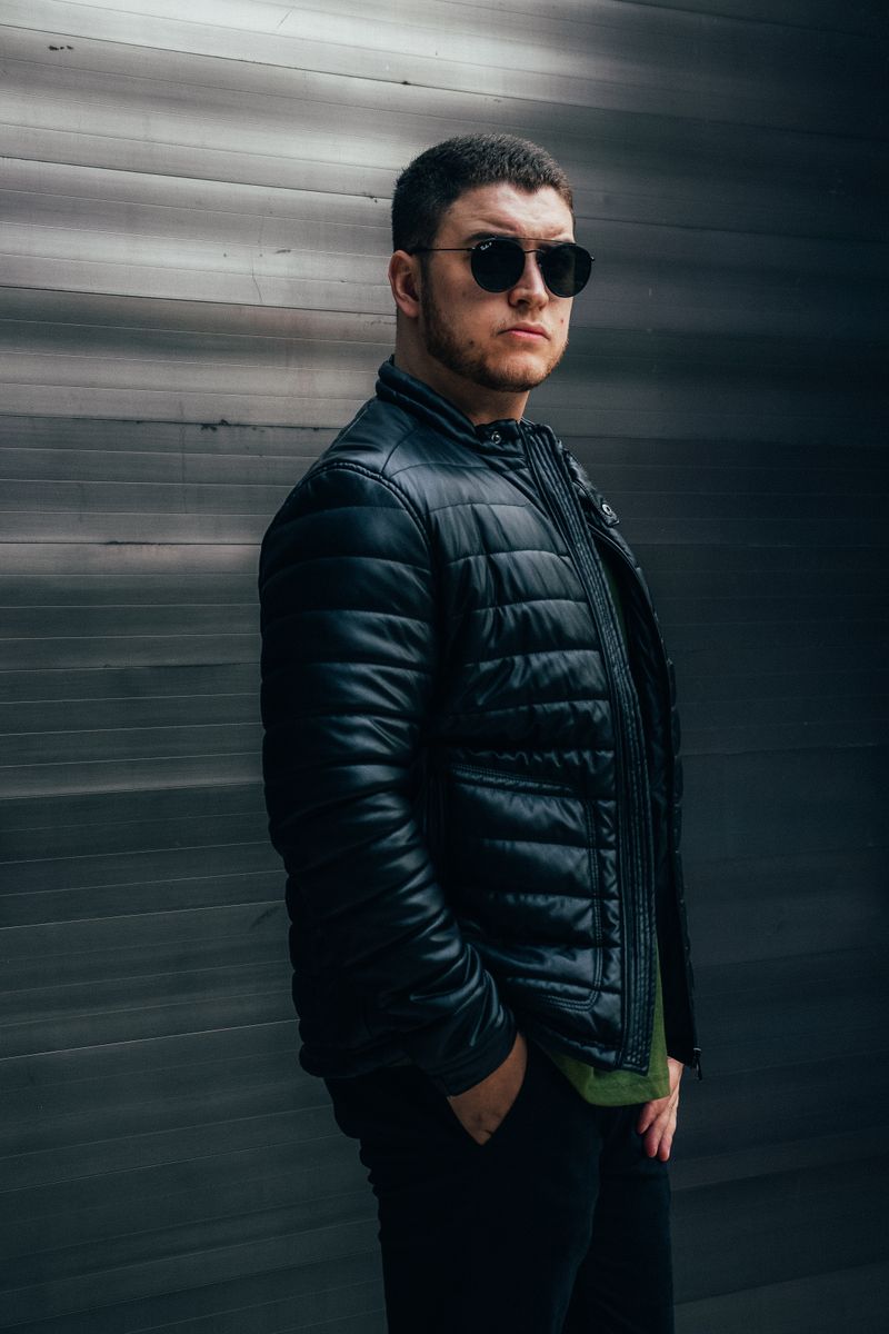 Portrait of a fashionable man posing with sunglasses and a black jacket.