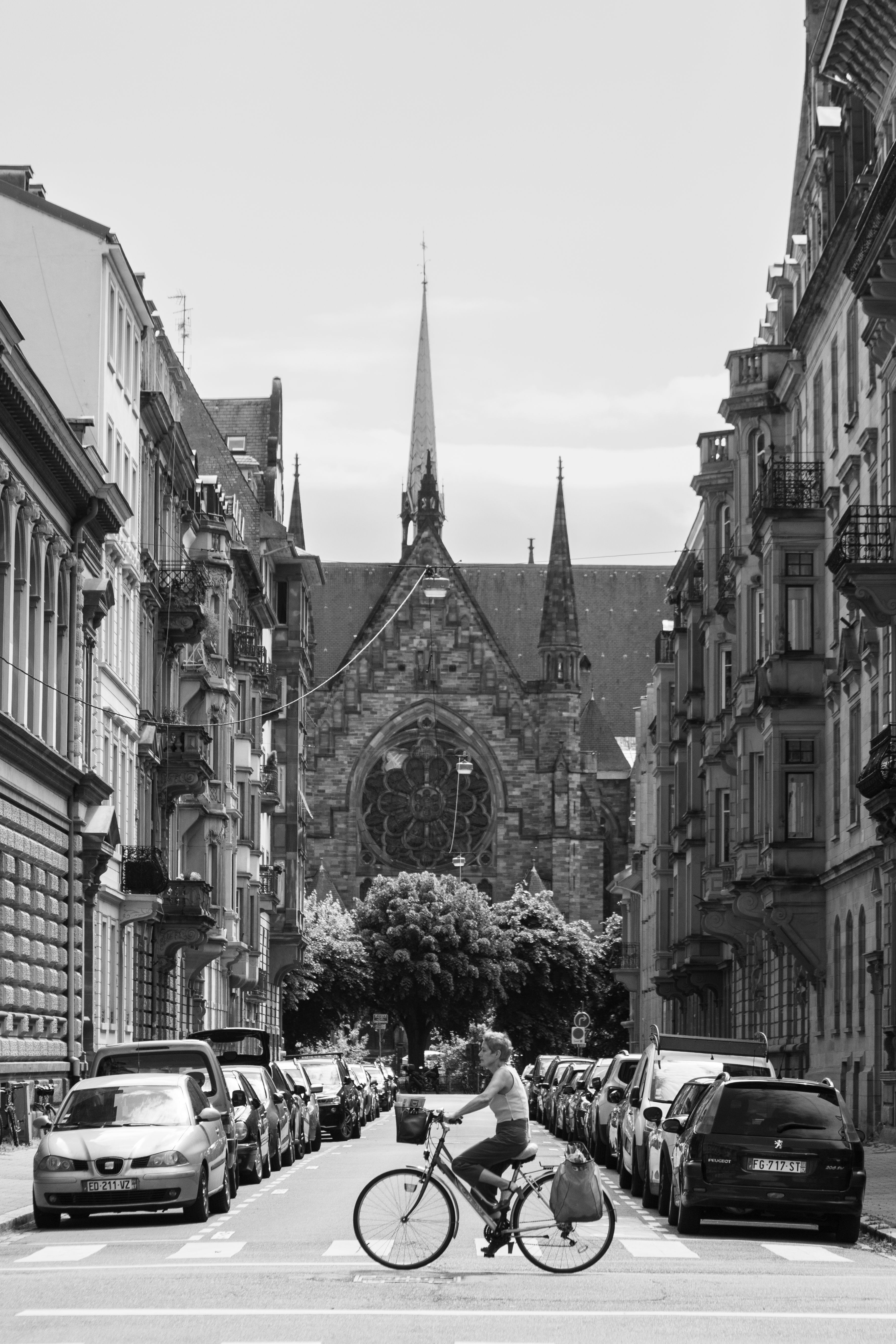 Black and white photo of a cyclist on a street in Strasbourg, featuring a cathedral backdrop.