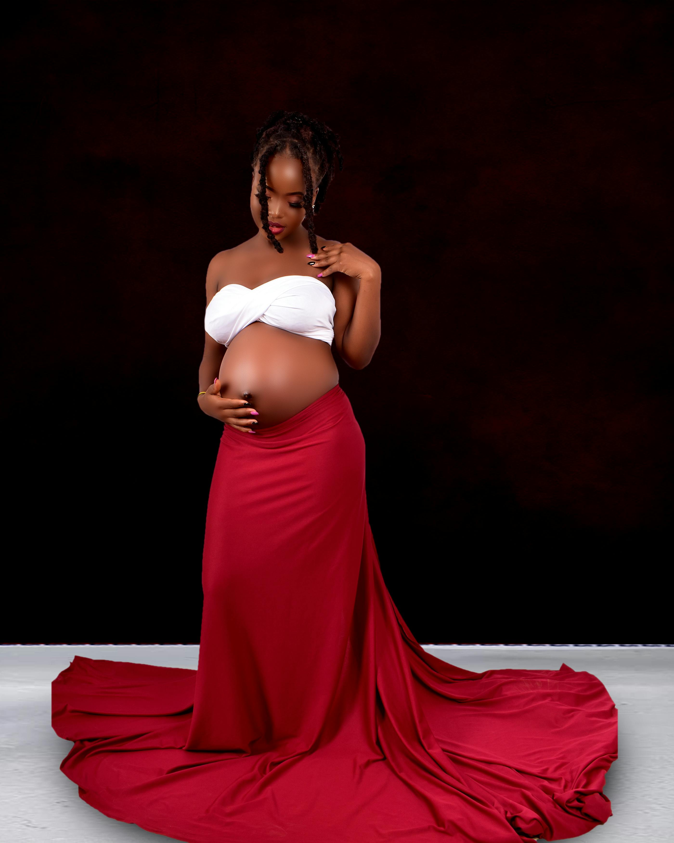 Pregnant woman in a red skirt and white top posing gracefully against a dark backdrop.