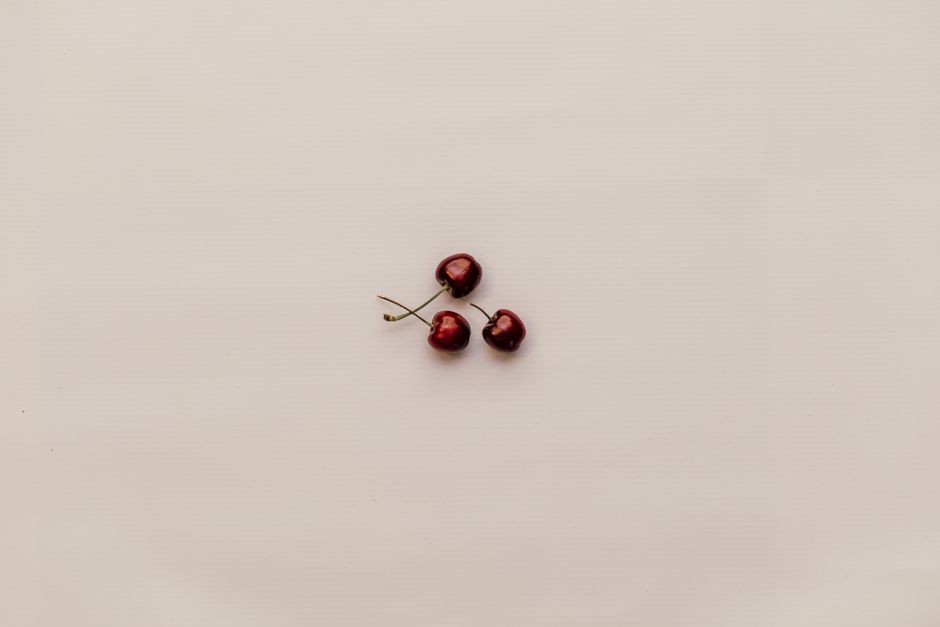 A minimalist composition featuring three ripe red cherries on a white background.