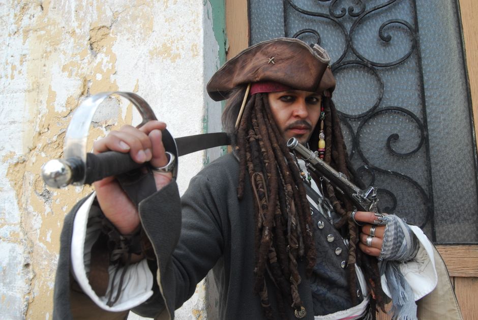 Pirate cosplay enthusiast poses with sword and hat at indoor location.