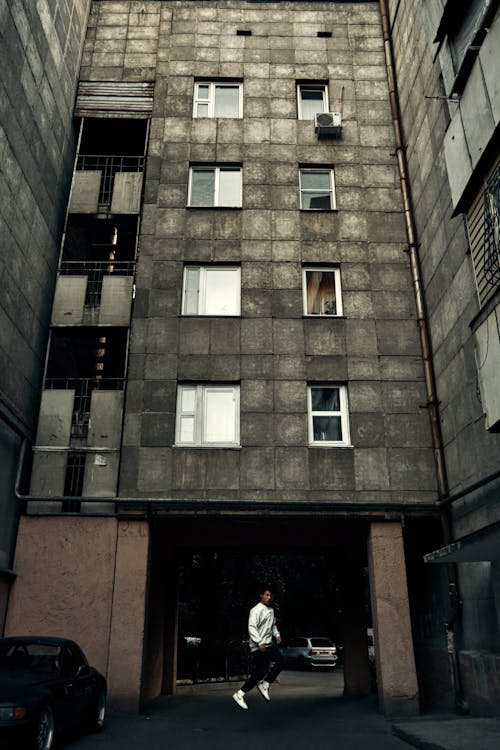 Free Man in Black Jacket Standing in Front of Brown Concrete Building Stock Photo