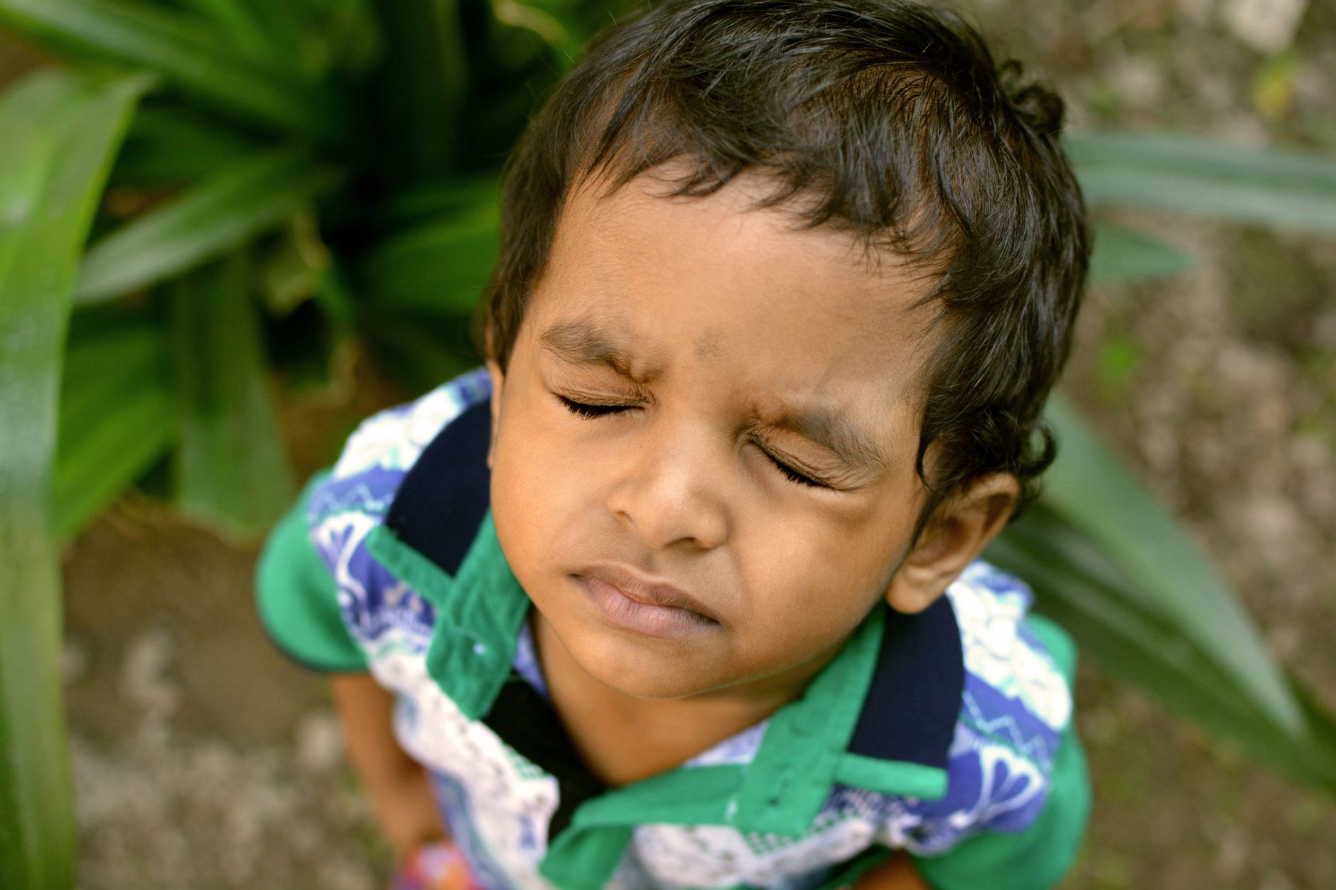 Close-up portrait of a young boy with eyes closed in an outdoor setting. Captures innocence and peacefulness.