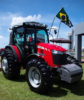 Vibrant red tractor showcased at an outdoor agricultural fair with a Brazilian flag in the background.